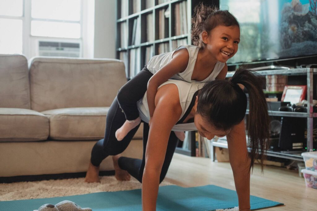Child on her mothers back while she tries to do yoga in the living room