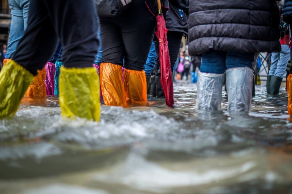 A crowd of people walking through flood waters that are almost up to their knees