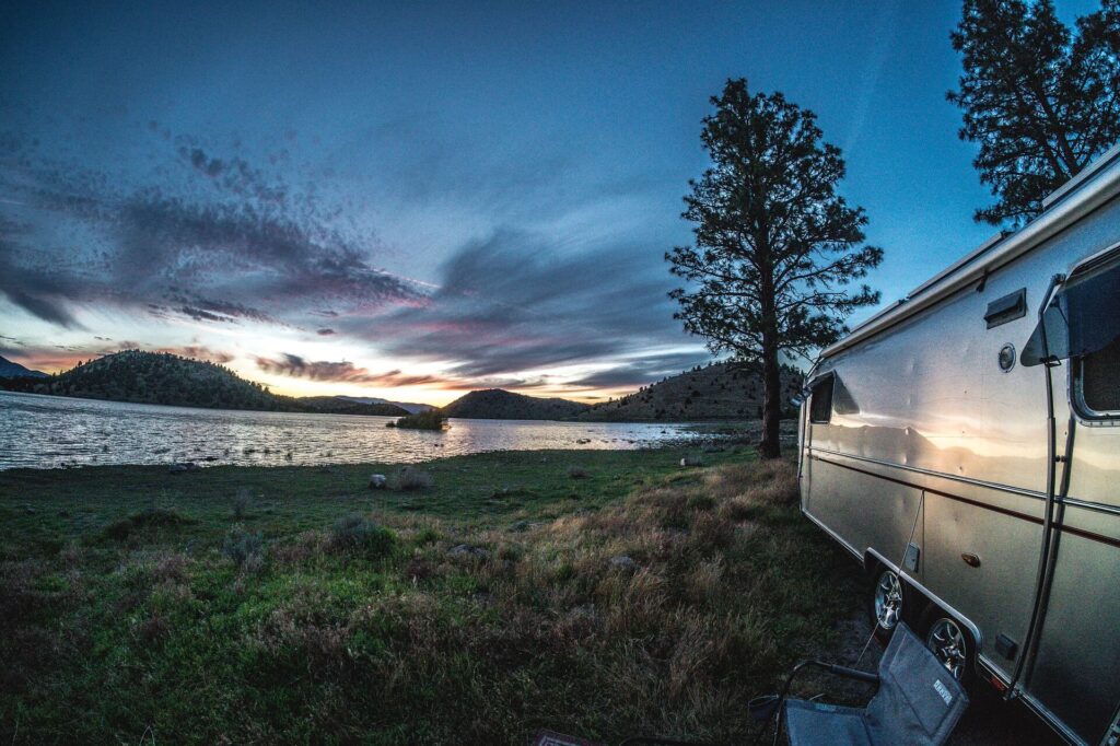 An RV trailer parked next to a lake at sunset.