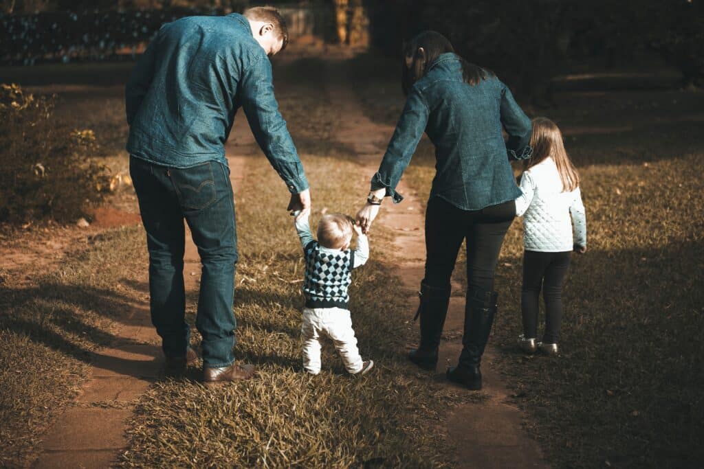 parents holding baby's hands as it learns to walk