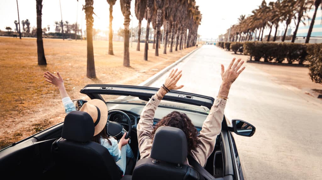 two people in convertible with arms raised