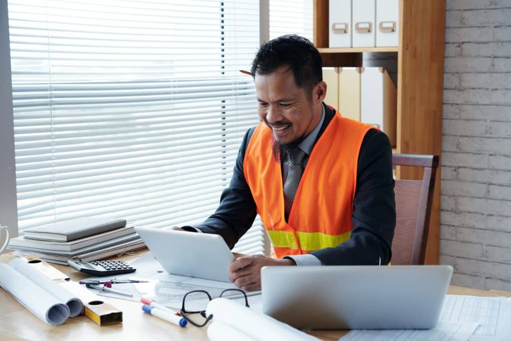 contractor in orange vest using laptop in office