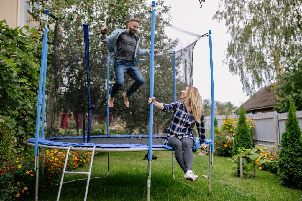 man jumping on trampoline with safety net while woman sits on frame