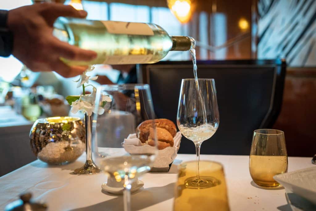 server’s hand pouring wine into glass at restaurant table