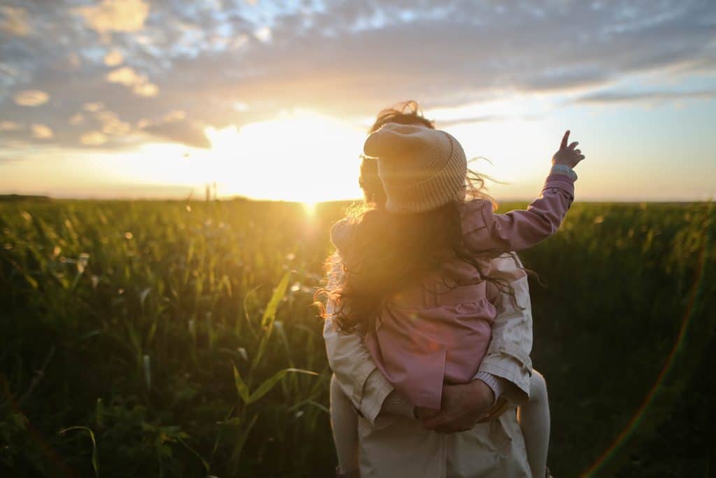little girl on mom's back in field during sunset