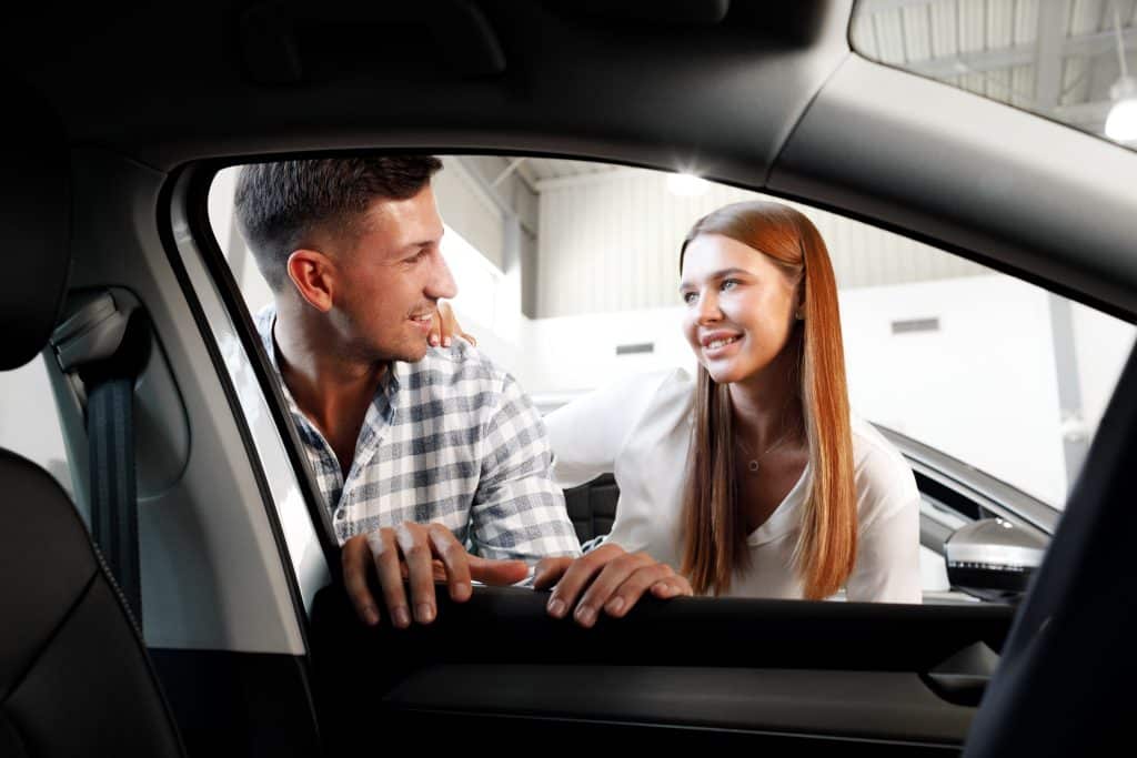 couple looking into car window while shopping at dealership