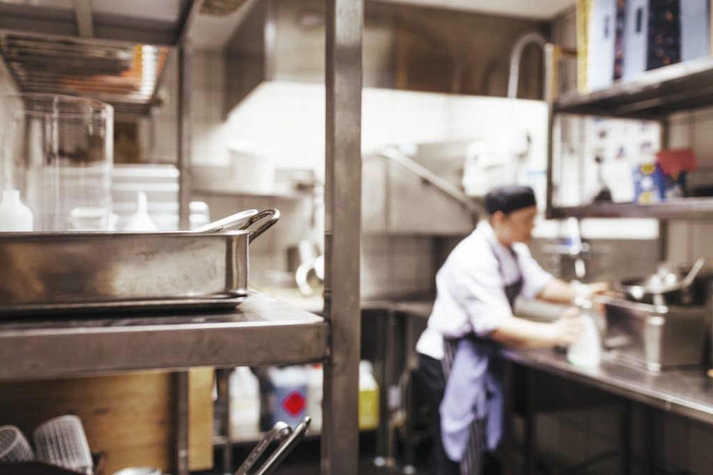 Close-up of shelf with chef working in background at commercial kitchen counter
